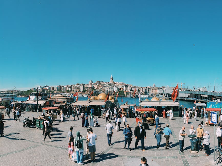 People exploring the lively Eminönü waterfront with Galata Tower in the background on a sunny day.