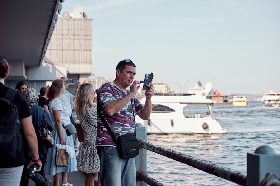 Tourists gather by the Bosporus in Istanbul, capturing memories with their phones on a sunny day.
