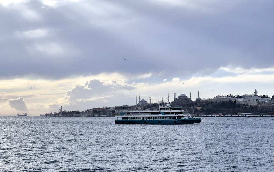 Ferry crossing the Bosphorus with Istanbul's iconic skyline in the background under a cloudy sky.